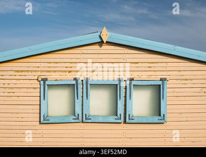 Facciata simmetrica di una capanna in legno dipinta di giallo che presenta una fila di tre finestre quadrate con cornice blu a Hunstanton, Norfolk, Inghilterra Foto Stock