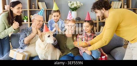 Famiglia felice che festeggia il compleanno a casa con torte a lume di candela e cane Labrador Foto Stock