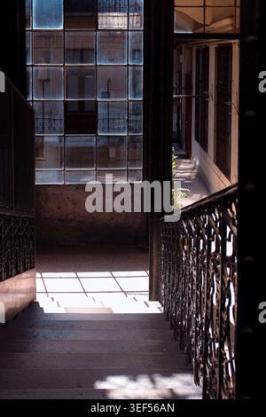 Budapest, Ungheria: Luci e ombre soffuse in uno storico cortile residenziale. Finestra industriale e dettagli in ferro battuto nell'appartamento. Foto Stock