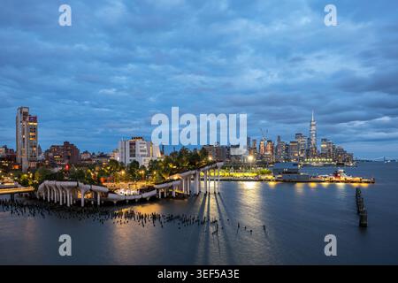 Splendida vista aerea dell'ora blu del parco urbano di Little Island e dello skyline illuminato di Lower Manhattan che si riflette sul fiume Hudson, New York Foto Stock