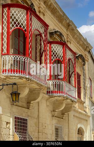 Malta, Mdina - 15 aprile 2025: Tradizionali balconi rossi maltesi (gallerija) aperti sulla storica casa cittadina di pietra, situata in via Villegaignon. Foto Stock