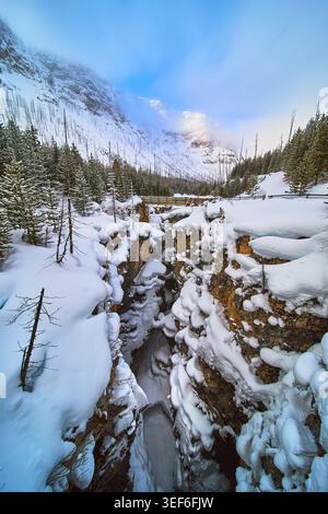 Snow Covered Canyon e Frozen River con Pine Forest nel Winter Mountain Landscape Foto Stock