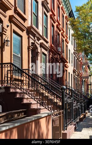 Tradizionali case in pietra arenaria con classiche ringhiere in ferro e alte fermate lungo una strada residenziale nel quartiere Harlem di Manhattan, New York. Foto Stock