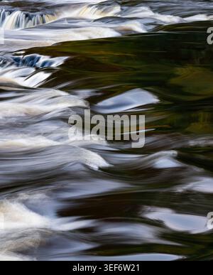 Primo piano astratto di acqua che scorre rapidamente con cascate visibili sullo sfondo Foto Stock