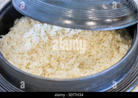 Riso integrale appena cotto in un tradizionale vaso di ghisa coreana. Il coperchio sollevato rivela grani dorati e umidi, catturando piatti genuini e salutari. Foto Stock