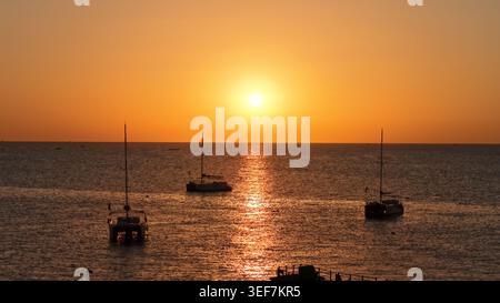 Vivace tramonto arancione sul mare calmo con barche a vela Foto Stock