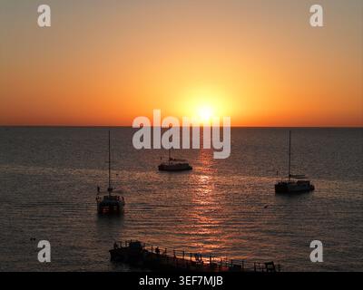 Tramonto sul mare calmo con barche a vela e molo Foto Stock
