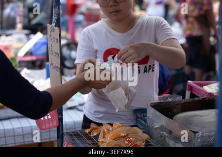 PHAYAO, THAILANDIA-APR 11, 2026: Donna che paga per beni, commercio culturale di strada in Asia, Close Up, Chiang Kham. Foto Stock