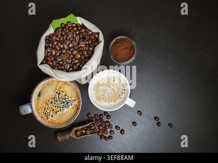 Tazze da caffè, chicchi di caffè e polvere macinata sulla superficie nera del tavolo. Posizione piatta Foto Stock