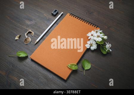 Cancelleria vuota su sfondo in legno. Quaderno arancione, matita, affilatrice e fiori Foto Stock