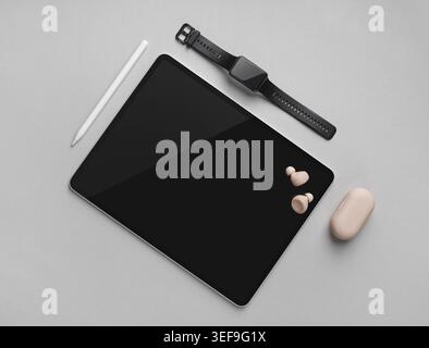 Tablet digitale con schermo nero vuoto, stilo, orologio intelligente e cuffie su sfondo grigio. Posizione piatta Foto Stock
