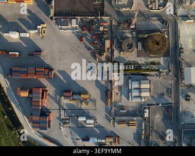 Vista aerea di un porto industriale con container impilati, macchinari pesanti e grandi avvolgicavo sotto la luce del sole ad Augusta, Sicilia, Foto Stock