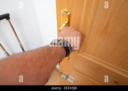 Mano di una persona che gira una maniglia di ottone accanto a una stampella e a un orologio intelligente Foto Stock