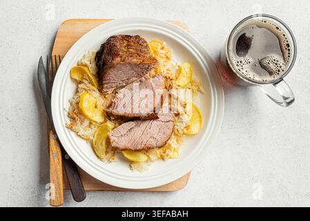 Maiale tedesco al forno con mele e crauti su sfondo bianco, vista dall'alto. Lombo di maiale cottura lenta con mele, cavolo, pasto bavarese dell'Oktoberfest Foto Stock