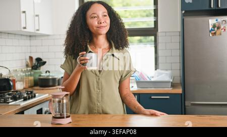 Giovane donna che si gusta un caffè nella cucina moderna, mattinata rilassata a casa Foto Stock