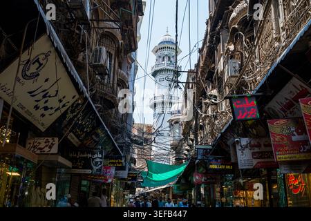 Bazar storico a Peshawar che mostra stradine strette e venditori con una torre sullo sfondo Foto Stock