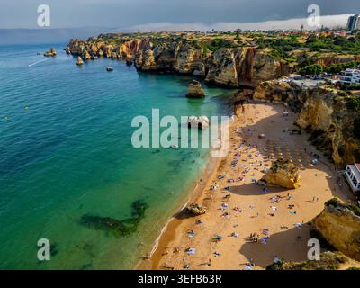 Vista al tramonto delle scogliere e della spiaggia sabbiosa dell'Algarve con gente che si gode la serata in acqua Foto Stock