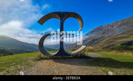 Il monumento della lettera e si erge sulle montagne con nuvole sopra nell'Ossezia del Nord, Russia, circondato da paesaggi naturali Foto Stock