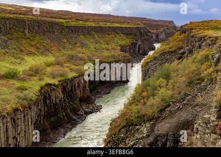 Scogliere aspre e colori autunnali nel canyon del fiume Hvit con il fiume che scorre attraverso strati di roccia vulcanica in Islanda Foto Stock