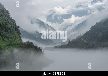 La nebbia scorre tra i verdi pendii e un tortuoso fiume in una valle di montagna del Sichuan occidentale, in Cina Foto Stock