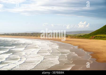 La luce della sera proietta lunghe ombre sulla spiaggia di Rhossili Bay con onde dolci e spiagge sabbiose a Swansea, Galles Foto Stock