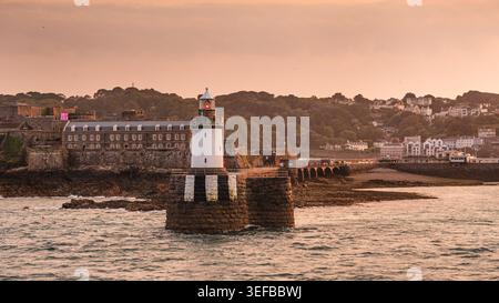Luce del tramonto che fa il bagno al faro e al Castle Cornet all'ingresso del porto di San Pietro a Guernsey Foto Stock