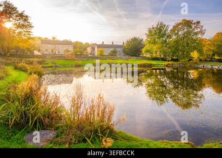 Riflessi in uno stagno del villaggio a Monyash in autunno con edifici e alberi in vista Foto Stock