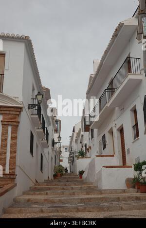 Ripida scalinata acciottolata fiancheggiata da edifici imbiancati e balconi in ferro battuto in uno stretto vicolo di Frigiliana, Andalusia, Spagna. Foto Stock