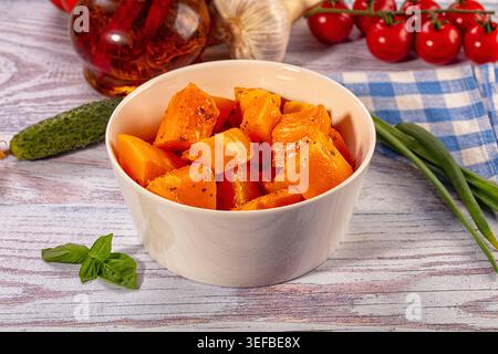 Ciotola di cubetti di zucca arrosto conditi con ingredienti freschi. Piatto vegetariano sano con pomodori, aglio ed erbe su fondo rustico in legno Foto Stock