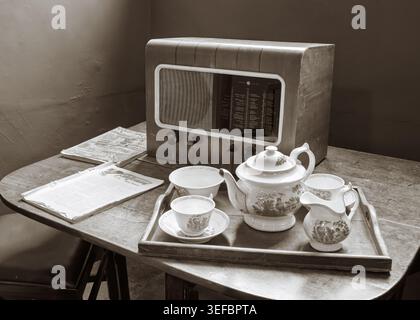 Uno spettacolo domestico vintage con un tradizionale tè bianco in porcellana su un tavolo accanto a una vecchia radio a Blickling Estate, Norfolk, Inghilterra Foto Stock