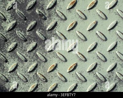 Vecchia struttura in metallo a piastre diamantate industriali grintose con vernice grigia resistente agli agenti atmosferici, macchie di ruggine e pesante usura superficiale, per superfici grintose architettoniche o meccaniche Foto Stock