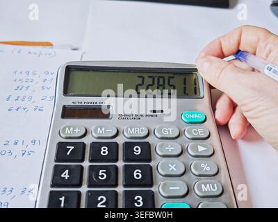 Kirov, Russia - 18 marzo 2026: La persona utilizza il calcolatore per il totale delle spese mensili durante la revisione delle ricevute e dei documenti per la pianificazione del budget domestico. Foto Stock