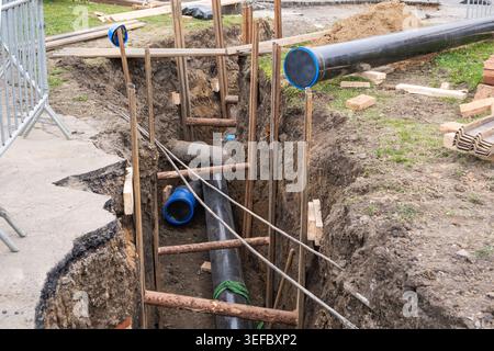 I tubi industriali pesanti con cappucci terminali blu sono collocati all'interno di una fossa di scavo supportata. Travi in legno e pali in metallo consentono di rivestire le pareti del terreno Foto Stock