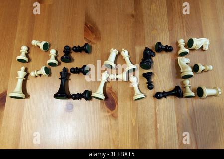 I pezzi degli scacchi, sia bianchi che neri, sono disposti su un tavolo di legno chiaro che forma la parola pace, simboleggiando concetti di risoluzione dei conflitti, diplomatico Foto Stock
