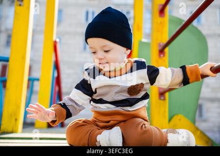 Baby sitter caucasico sulla piattaforma del parco giochi in un'area residenziale soleggiata. Infanzia e stile di vita attivo. Foto Stock