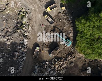 Vista aerea della miniera di sabbia di Tambang Pasir Merapi Kali Gendol con un escavatore che carica camion e lavoratori sul terreno a Kecamatan Cangkringan, Daerah Foto Stock
