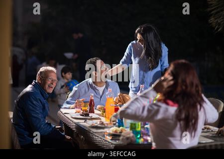 Famiglia multigenerazionale che condivide una calda cena di festa e chiacchiera a casa all'aperto Foto Stock