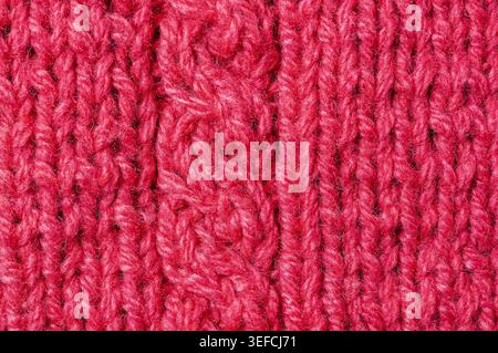 Vista dettagliata di un tessuto rosso a maglia spessa, calda e accogliente con intricati motivi di cavi e fibre di filati visibili Foto Stock
