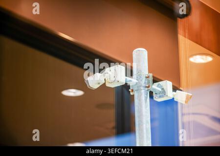 Primo piano di una telecamera di sicurezza montata su un palo metallico all'esterno di un edificio moderno con finestre in vetro, che enfatizza la tecnologia di sorveglianza e sicurezza i. Foto Stock