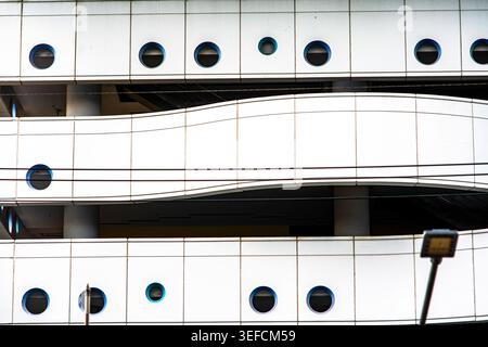 Questa immagine mostra l'esterno di un edificio moderno caratterizzato da una facciata liscia con finestre circolari e un balcone curvo, a dimostrazione di contemporaneità Foto Stock