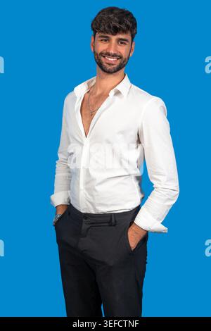 Uomo sorridente in piedi con le mani in tasca su sfondo blu Foto Stock