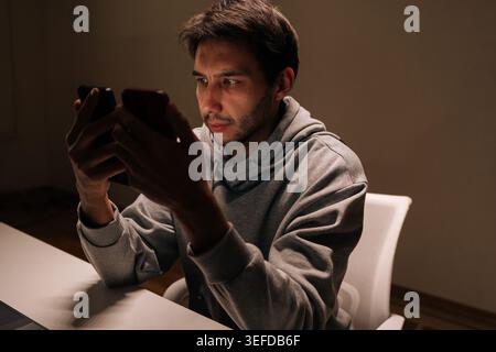Giovane concentrato che tiene e confronta due smartphone contemporaneamente, concentrandosi sul lavoro multitasking, sulla gestione di più dispositivi digitali e. Foto Stock