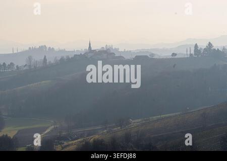 Strada di campagna tortuosa sotto il villaggio di collina nebbioso di Gerusalemme nelle colline vinicole di Ljutomer-Ormož in Slovenia. Foto Stock