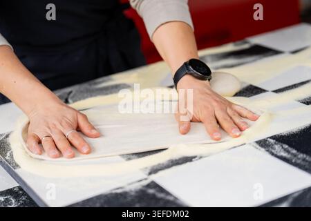 Processo manuale di modellatura dell'impasto per pizza italiana su un bancone bianco e nero, che illustra la produzione alimentare delle piccole imprese e l'abilità di cottura esperta Foto Stock