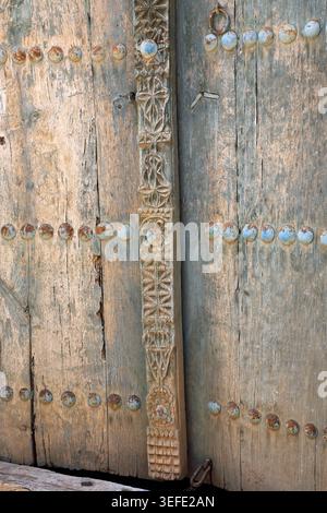 Primo piano di una porta in legno intagliata con borchie in metallo al Museo di storia vivente di Bait al Safah e al villaggio abbandonato al Sultanato di al Hamra in Oman Foto Stock