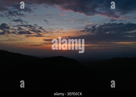 Un tramonto mozzafiato proietta calde sfumature dorate all'orizzonte sopra le colline ondulate e sagomate, con spettacolari nuvole dipinte in arancione e viola Foto Stock