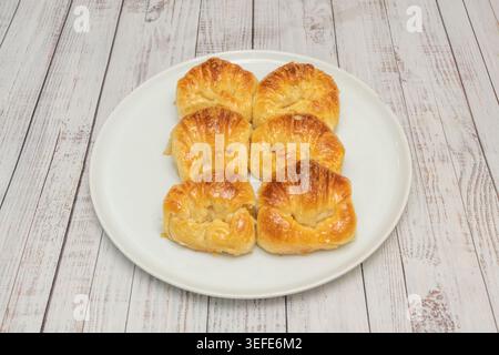 Sei dolci a spirale dorati lucidi disposti su un piatto ovale bianco su una superficie in legno imbiancato. Foto Stock