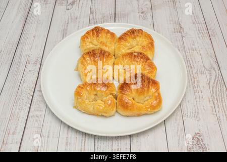 Sei dolci a spirale dorati lucidi disposti su un piatto ovale bianco su una superficie in legno imbiancato. Foto Stock