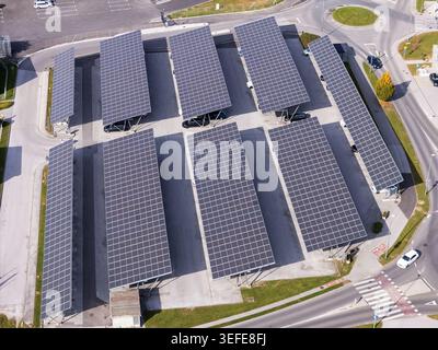 Vista aerea dei pannelli solari installati su un parcheggio con auto parcheggiate e infrastrutture urbane in Slovenia. Foto Stock