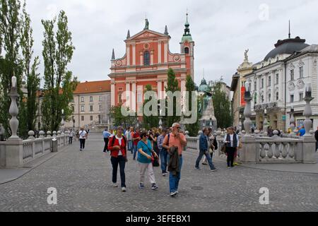 I turisti camminano attraverso lo storico Ponte triplo verso Piazza Prešeren e la Chiesa francescana dell'Annunciazione a Lubiana, Slovenia Foto Stock